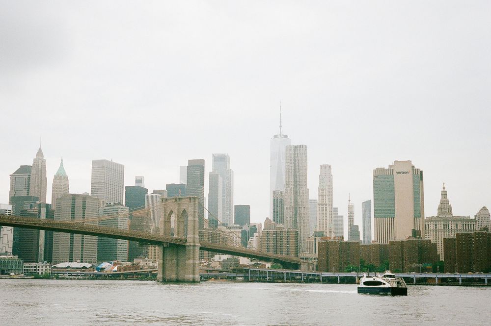 View of Manhattan skyline and Brooklyn Bridge with boat on East River on an overcast day.