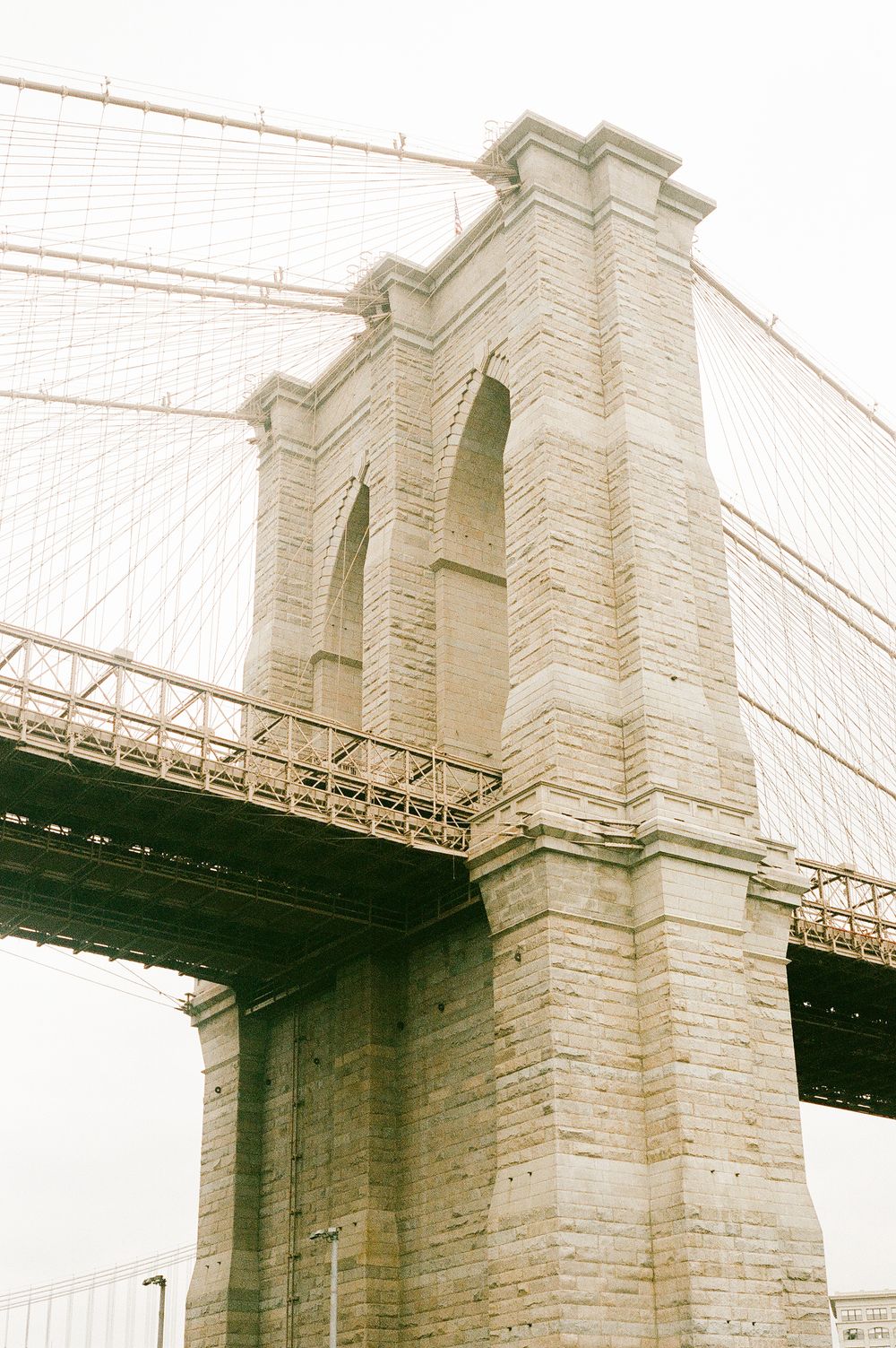 Historic stone pillars and arches of the Brooklyn Bridge stand tall against a bright sky, showcasing its iconic design.