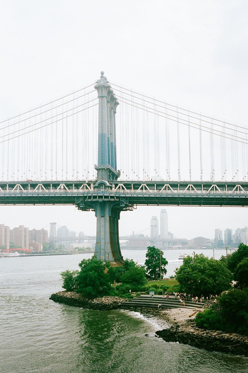 View of the East River and Manhattan Bridge support tower from Brooklyn Bridge Park on a foggy day in New York City.