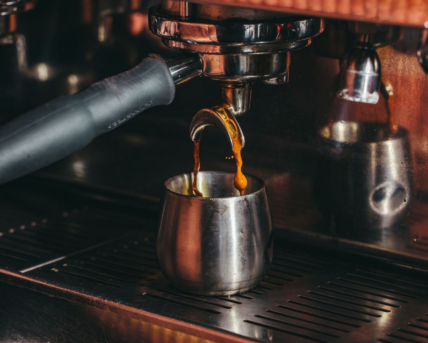 Espresso shot being pulled from a commercial coffee machine into a metal portafilter.
