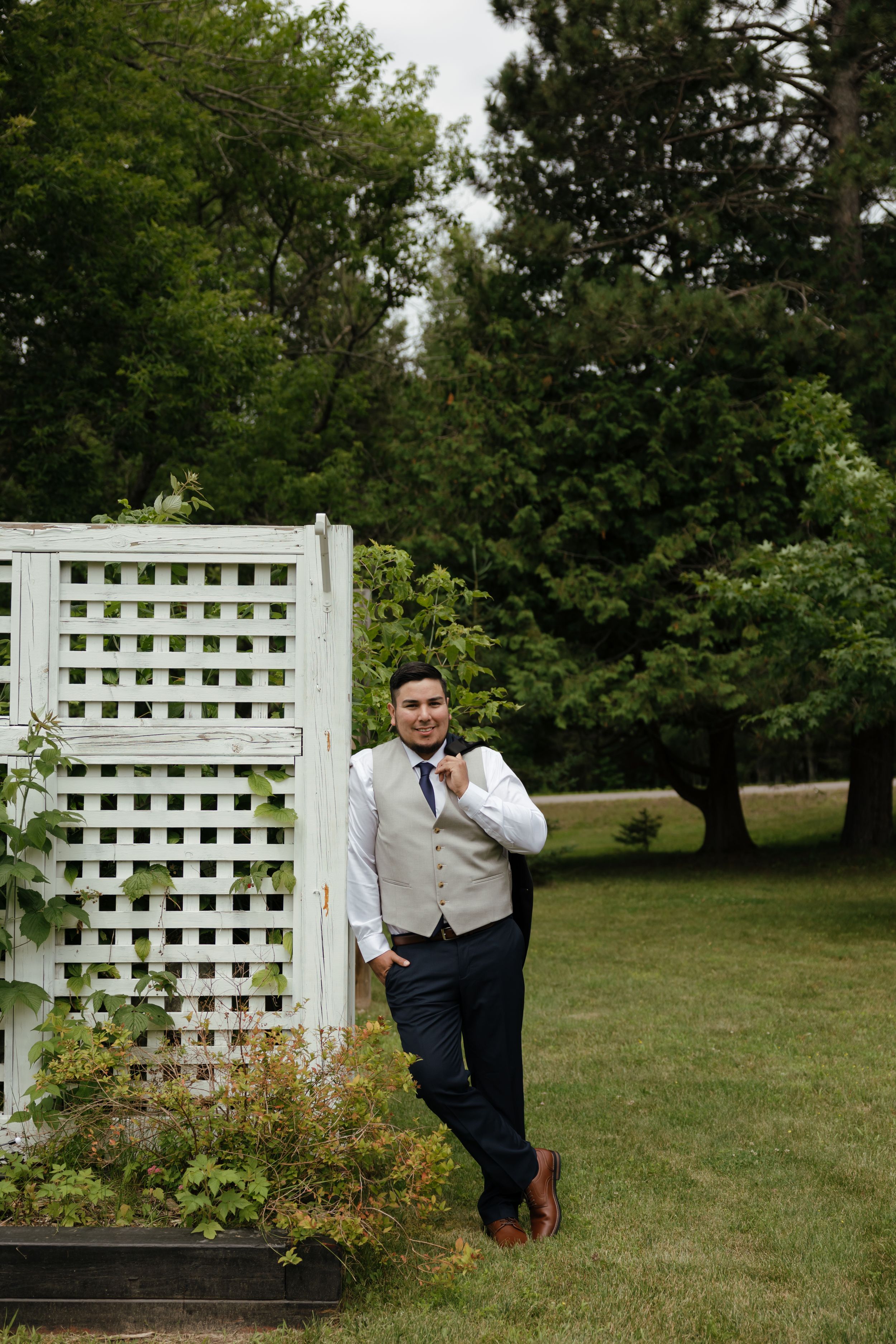 White lattice garden arbor structure serves as a rustic backdrop in an outdoor garden setting amidst green trees.