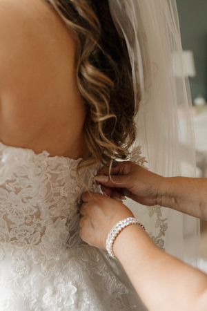 Close up of intricate lace details and buttons being fastened on a wedding dress.