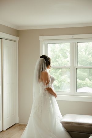 A wedding dress is beautifully displayed in a bright room with natural light streaming through large windows.