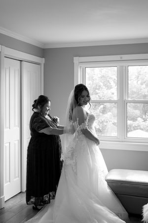 A wedding dress preparation scene in a bright room with multiple windows and grey walls.
