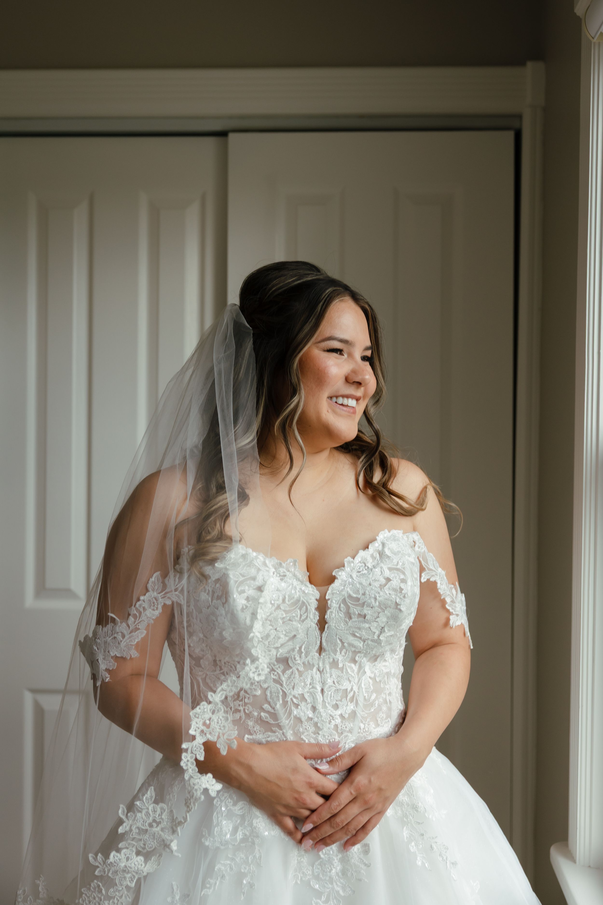 A detailed view of a white wedding gown with delicate lace details and off-shoulder design in natural lighting.