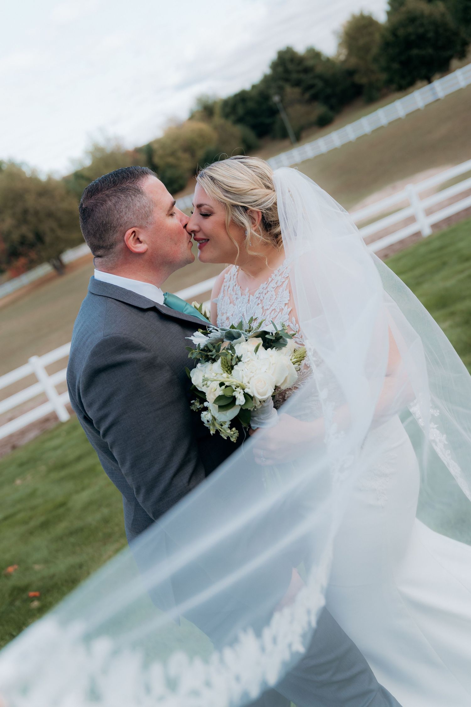 A romantic wedding portrait with the bride's veil flowing in the wind against a countryside backdrop.