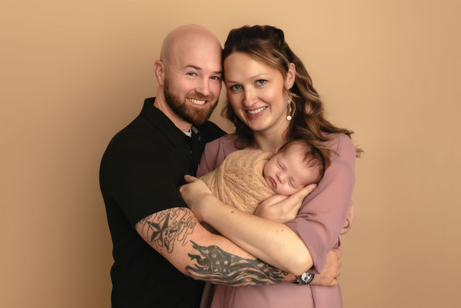 New parents cradle their sleeping newborn daughter, who is wrapped in a warm, beige blanket, during Charlottesville studio baby session.