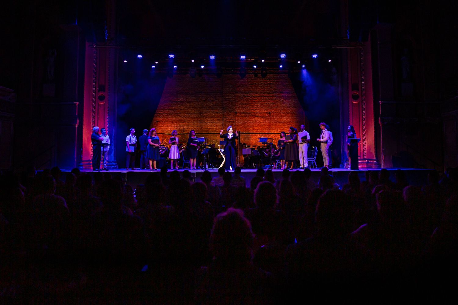 Stage performance with performers silhouetted against blue and red theatrical lighting.