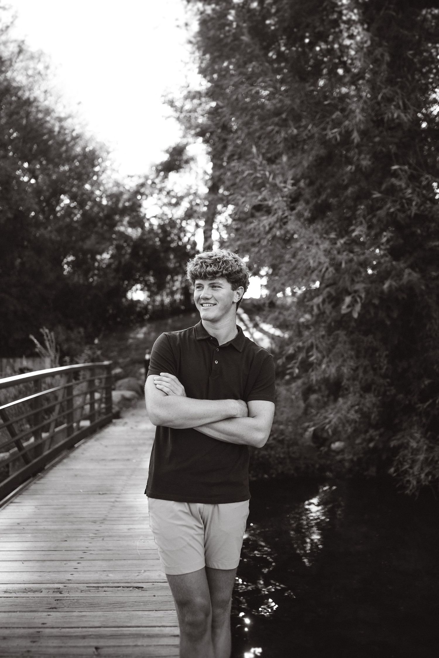 Black and white photo of person standing on wooden bridge in nature setting.