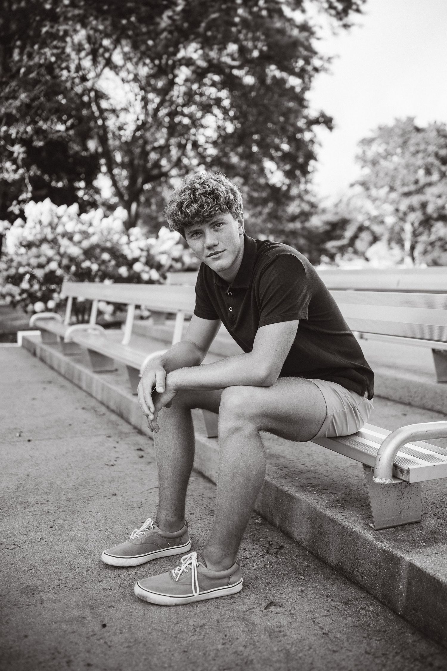 Person in dark polo and shorts sits on concrete steps in black and white photo.