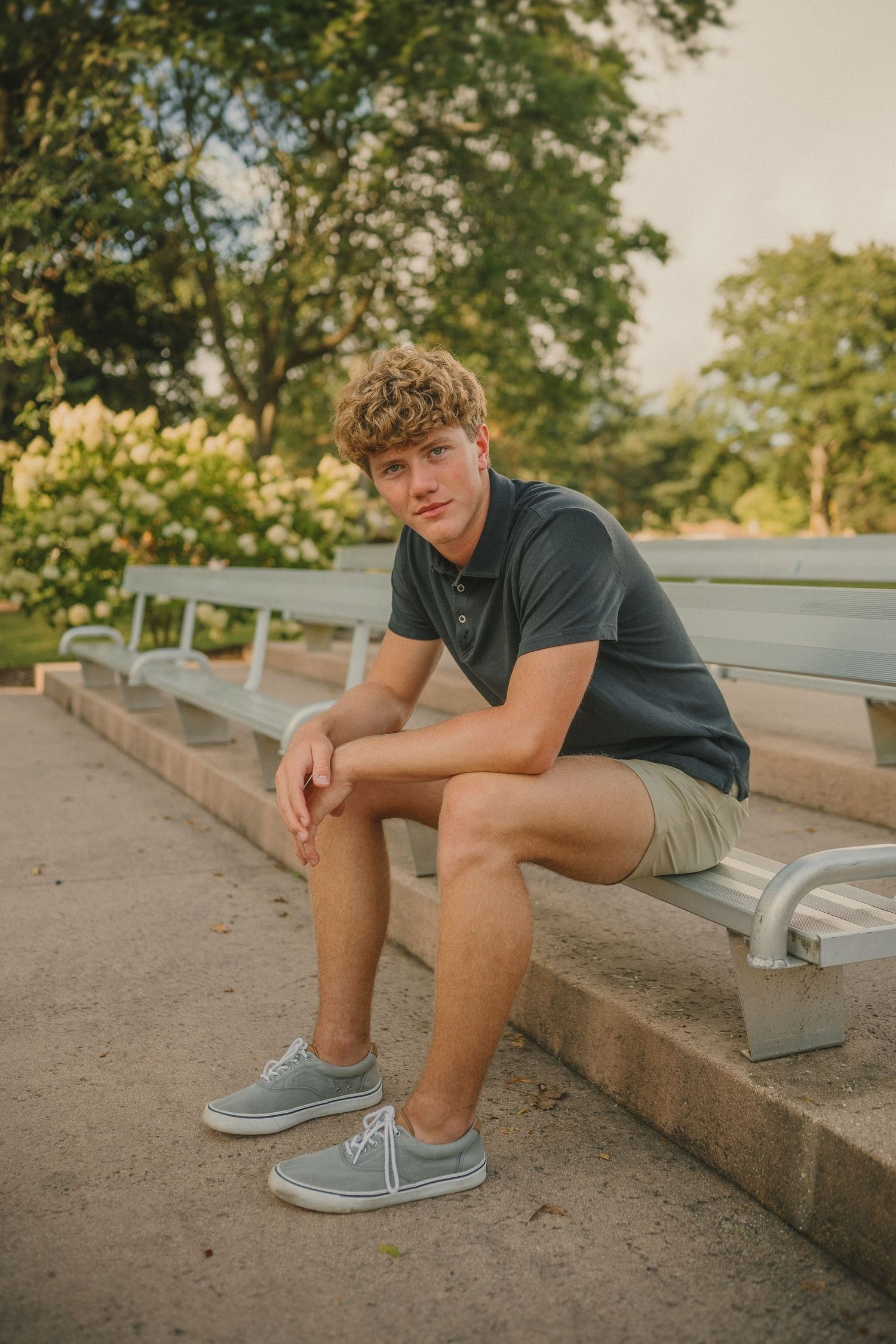 Person in navy polo and khaki shorts relaxes on outdoor steps during golden hour.