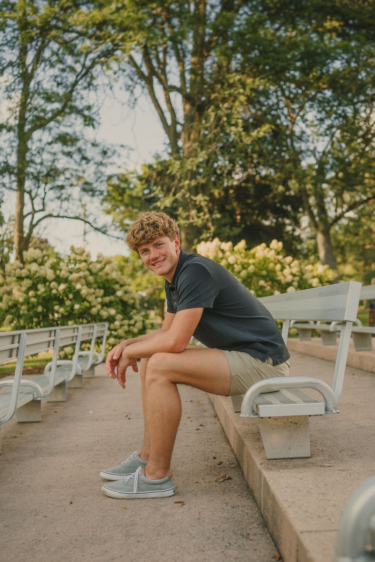 Casual outdoor portrait on park bench during golden hour with trees in background.