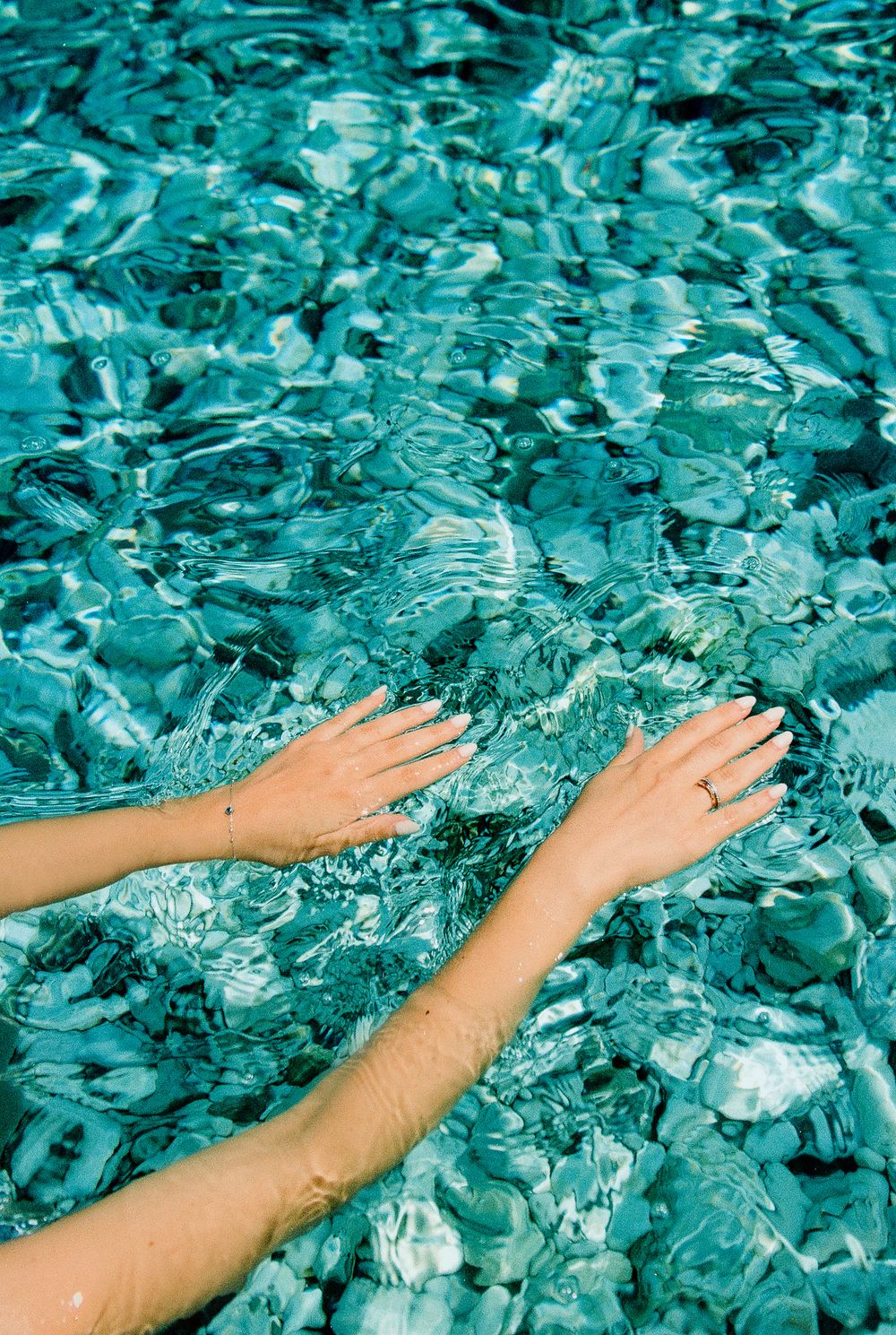 Hands submerged in clear shallow water over rocky seabed.