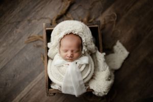 Peaceful newborn swaddled in white knit blanket resting in rustic wooden container.