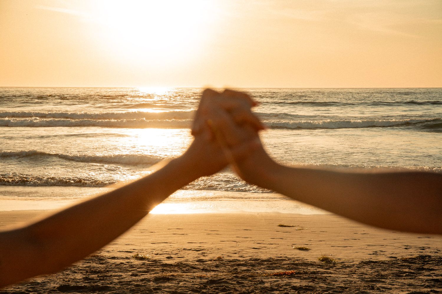 Two silhouetted hands joining together in a high-five gesture against a golden sunset beach background.