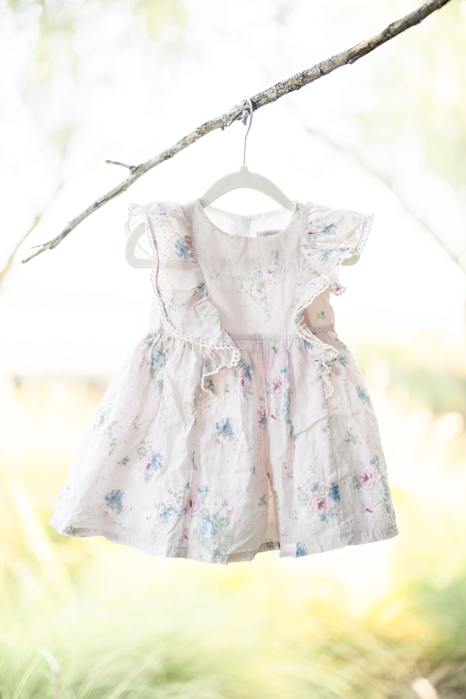 White floral baby dress hanging from a tree branch in soft natural light.