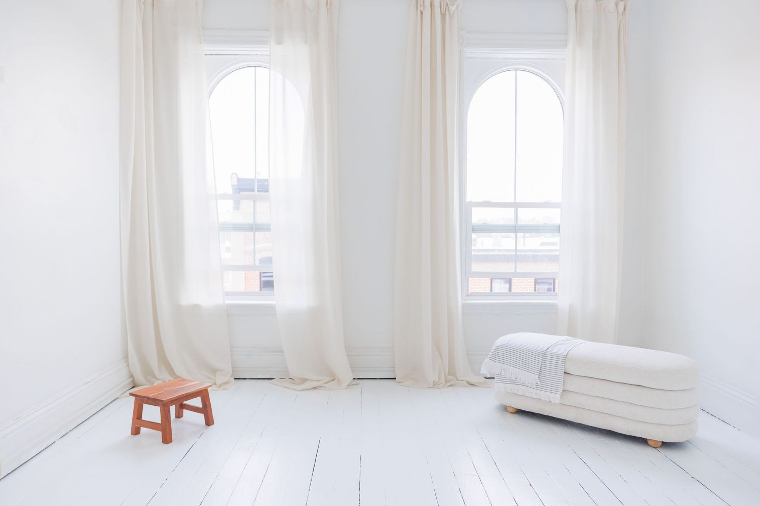A minimalist white room interior with wooden stool, gray carpet, cast iron radiator and white paneled door.