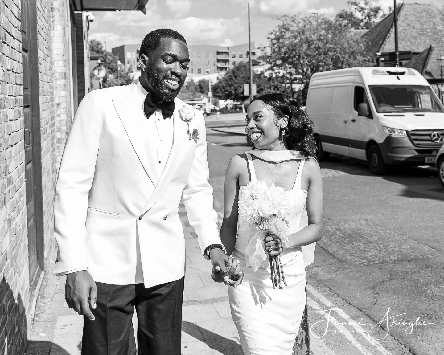 Newly wed bride and groom walk and chat on the pavement of a city street.
