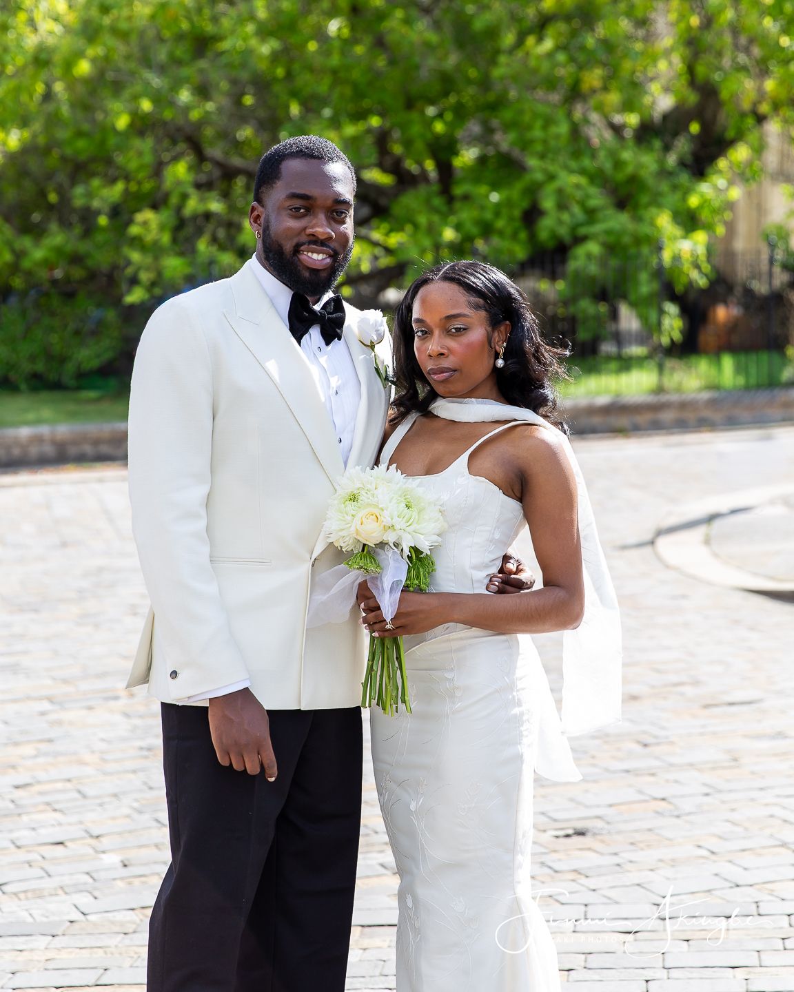 A newly wed bride and groom share a special moment outdoors at their elegant wedding wearing white attire and holding a bouquet.