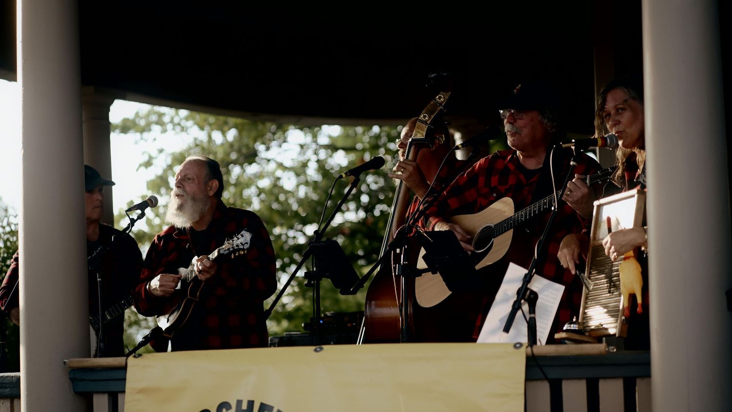 Bluegrass musicians performing on an outdoor gazebo stage with guitars and banjo at a folk music festival.