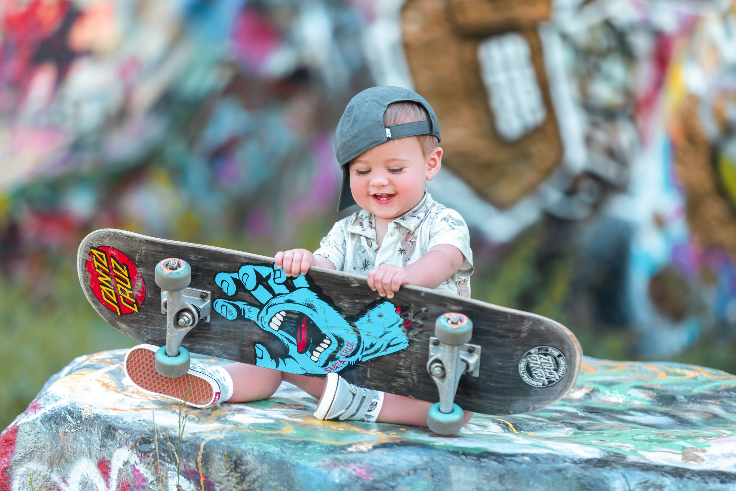 Young child in a cap examining a skateboard with blue details against a colorful blurred background.