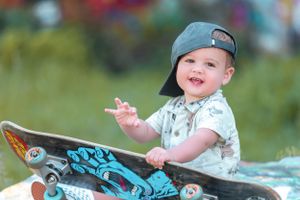 Young child in backwards cap sitting joyfully with a blue skateboard outdoors.