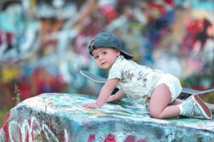 Small child wearing a cap crawls on colorful graffiti-covered surface with dreamy bokeh effect in background.