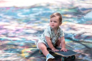 Young child sits on skateboard against vibrant multicolored background with soft focus effects.