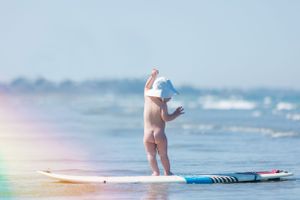Toddler stands on a paddleboard in natural light at the beach on a sunny summer day.