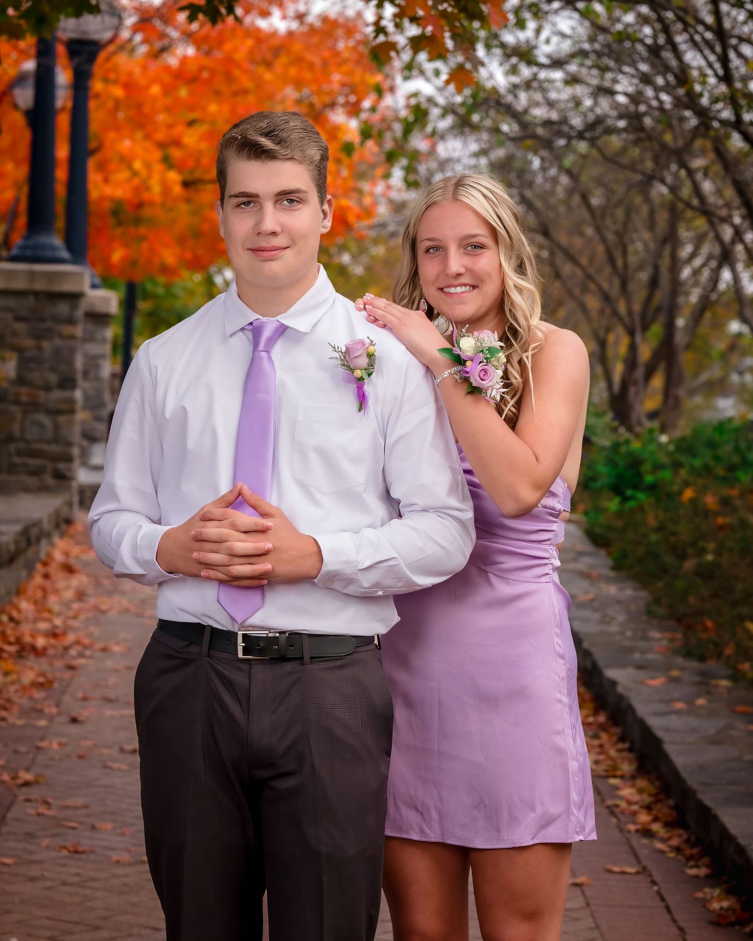 A couple poses on a stone walkway during autumn with vibrant orange foliage in the background.