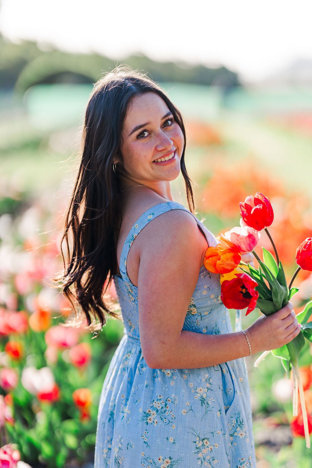 A floral light blue dress stands out in a vibrant red tulip field on a sunny spring day.Simi Valley Senior Photographer