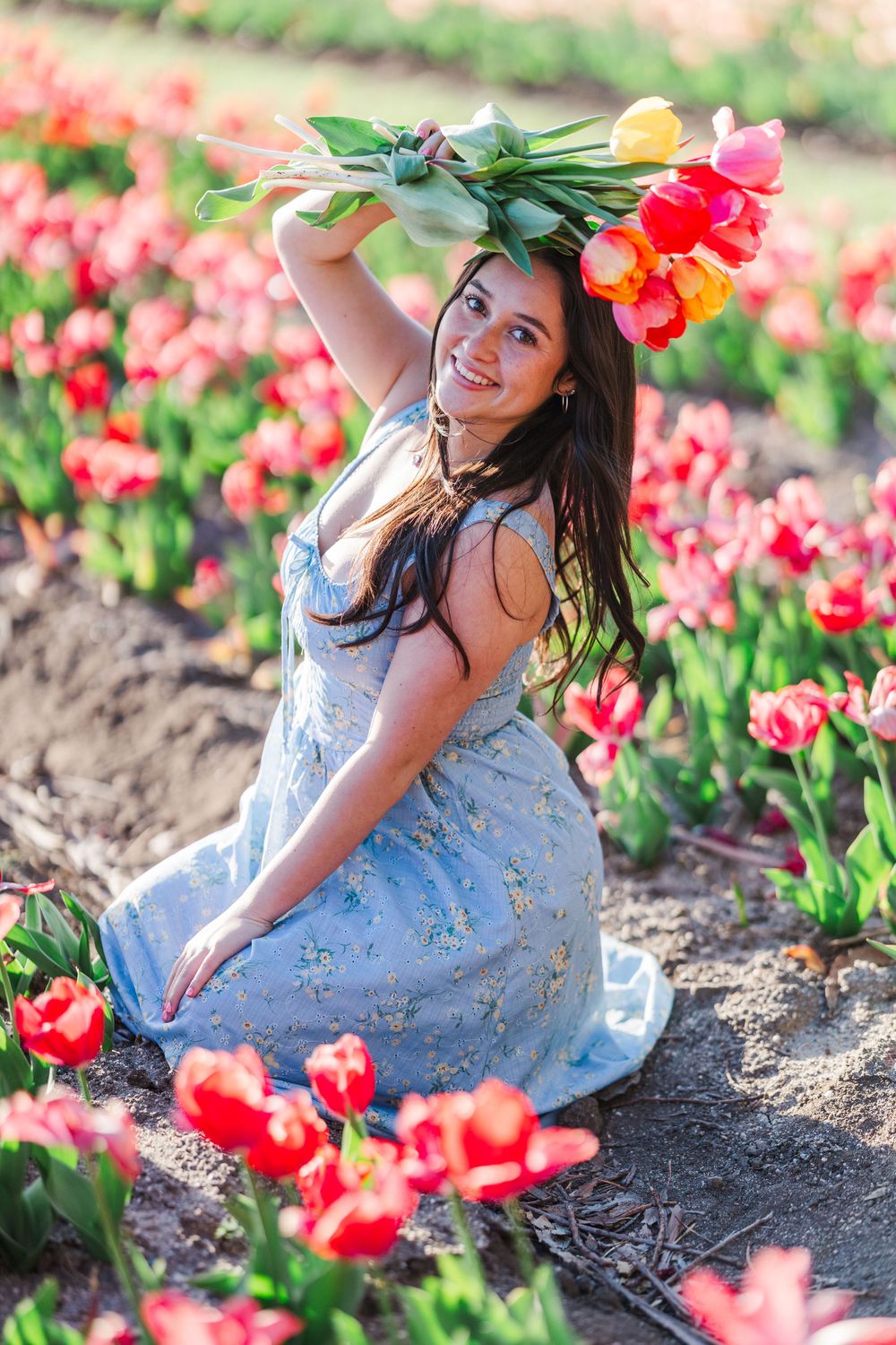 A person in a blue floral dress poses among vibrant red tulips on a sunny spring day at a flower field. Simi Valley Senior Photographer