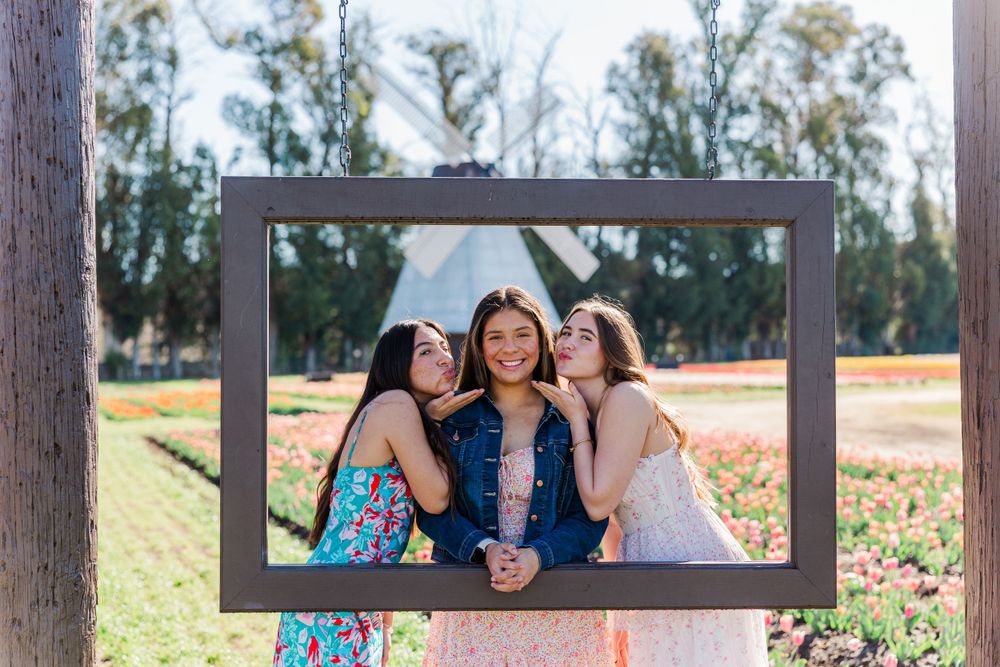 Three friends pose together through decorative photo frame in outdoor garden setting.Simi Valley Senior Photographer