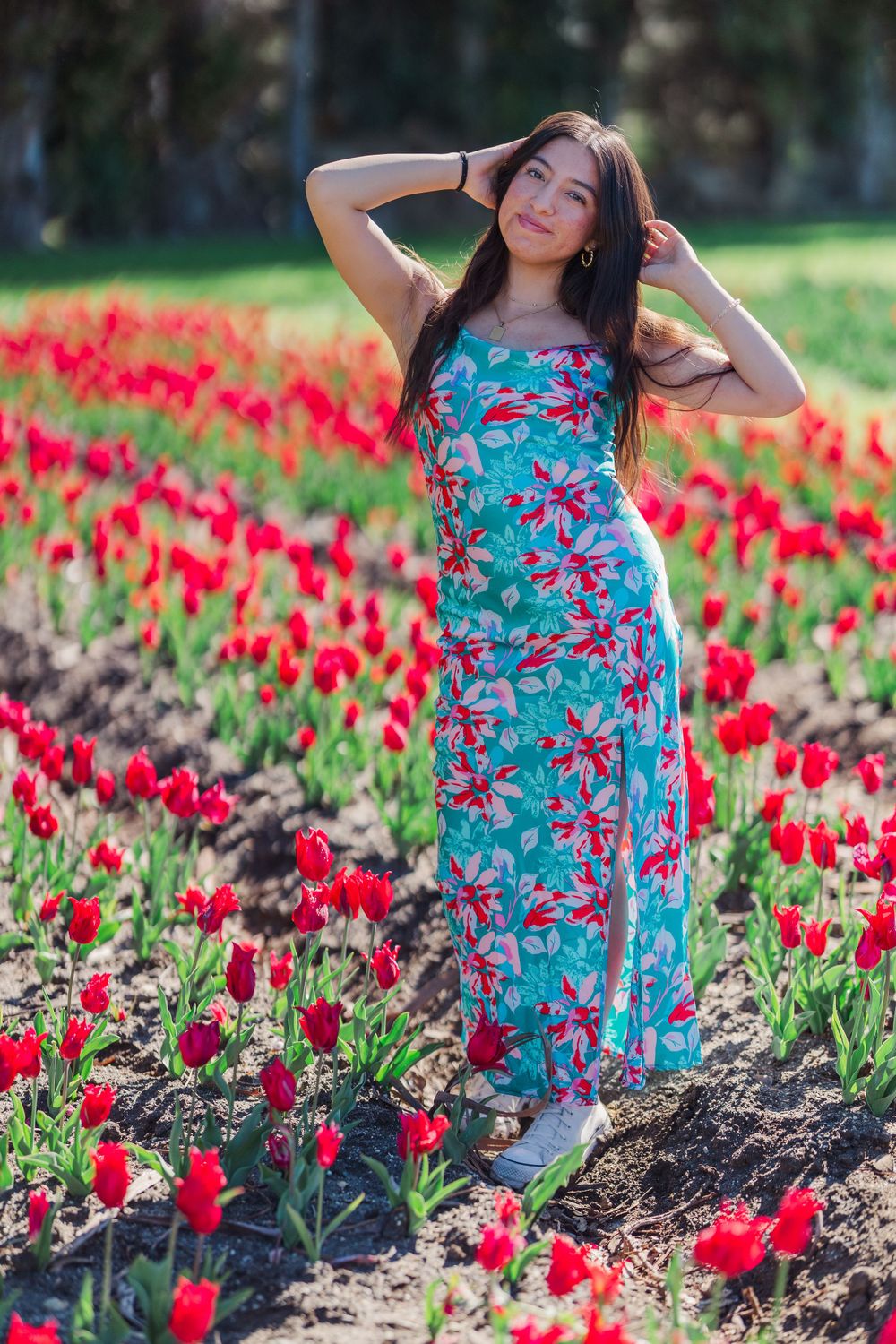 Person in floral blue dress poses among vibrant red tulips in sunny garden setting. Senior Photographer in Simi Valley CA