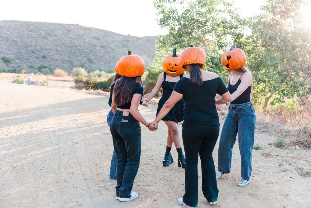 Friends walking together on a dirt path wearing pumpkins on their heads in a playful outdoor autumn scene. Simi Valley Photographer
