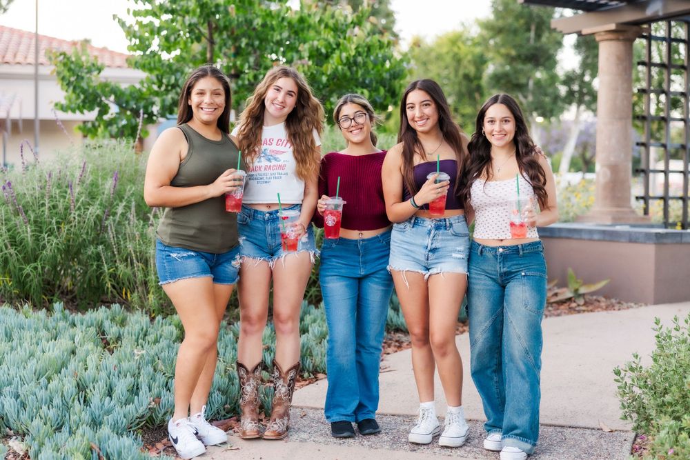 Five students standing together and smiling outside path with green plants and architecture visible. Simi Valley Senior Photographer