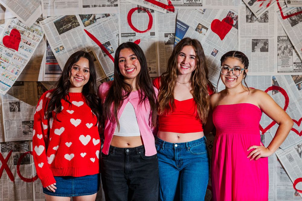 A group poses in festive red and pink outfits against a wall decorated with heart cutouts and paper decorations.Simi Valley Photographer
