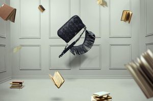 A black fringed handbag floats mid-air surrounded by flying open books in a grey paneled room.