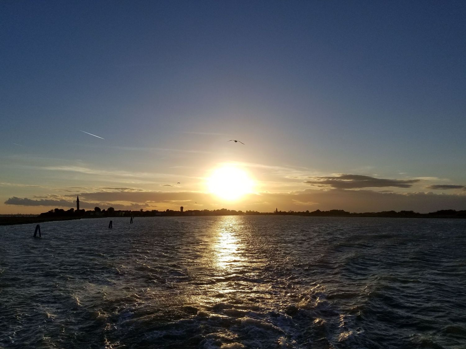 Stunning sunset over water with silhouetted cityscape and boats in the distance.