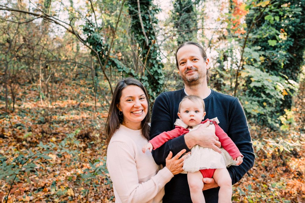 Three people pose together in a forest setting with fall foliage in the background.