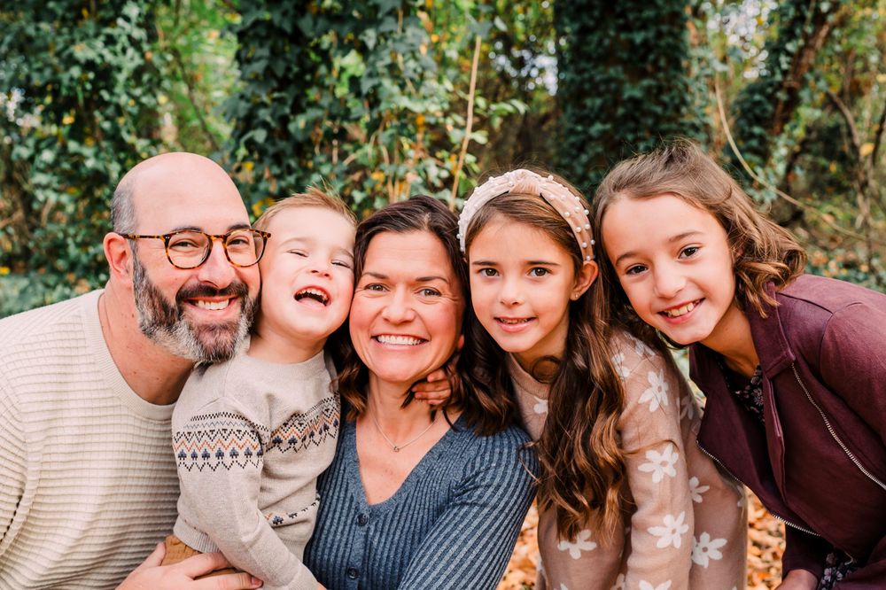 A loving family group hugs close together while posing outdoors in a natural setting with greenery in the background.
