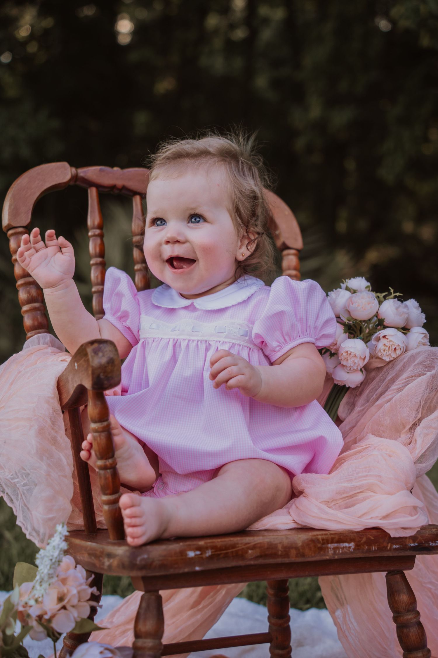 Pink outdoor photo setup featuring a vintage rocking chair, flowers, and delicate lace decorations on white blankets.