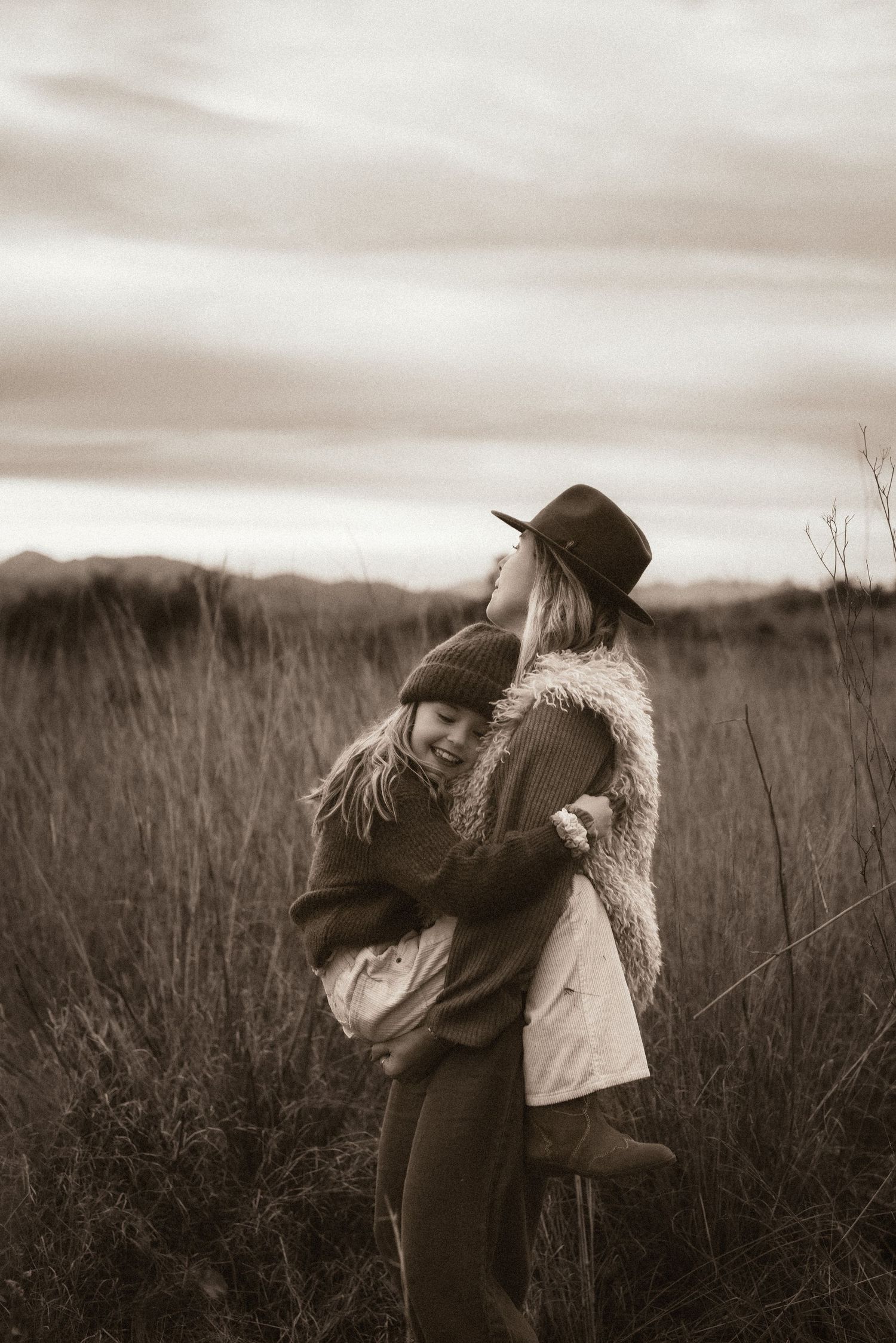 A tender black and white moment captured in a serene field with tall grass and moody sky in Javea Photography, Javea photographer