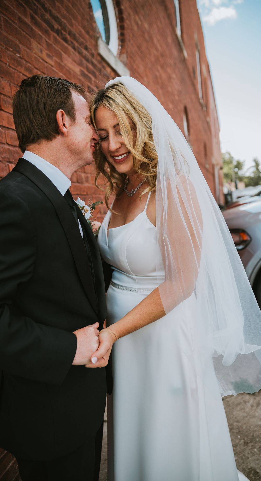 A couple shares an intimate moment on their wedding day against a rustic brick wall backdrop.