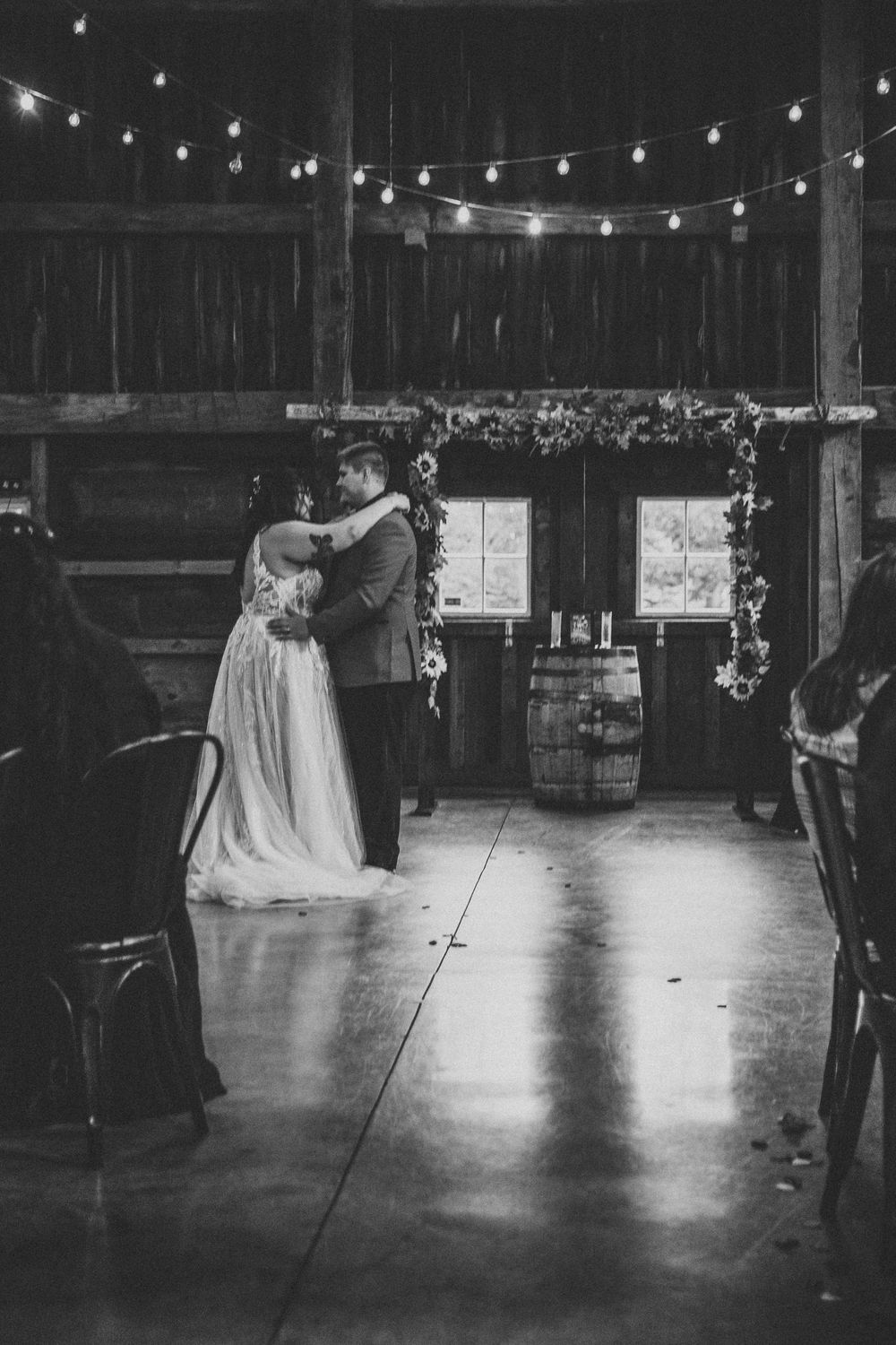 A romantic barn wedding reception with string lights overhead as a couple dances intimately in black and white.