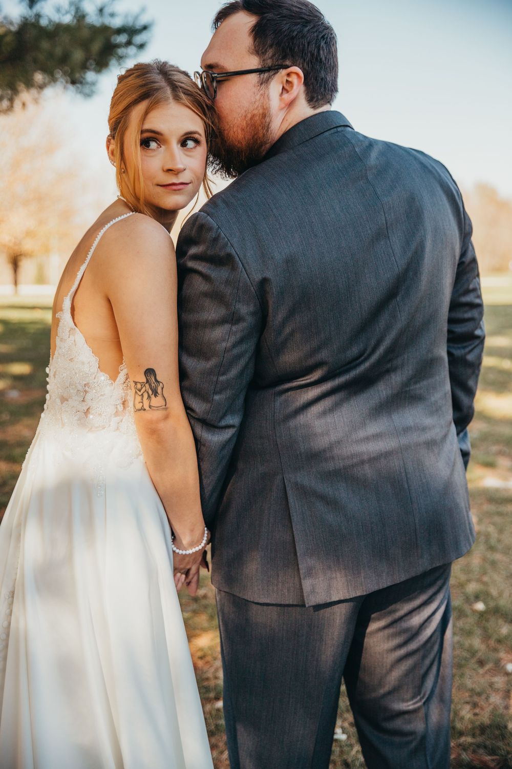 A romantic outdoor wedding photo at sunset featuring a couple in formal wedding attire.