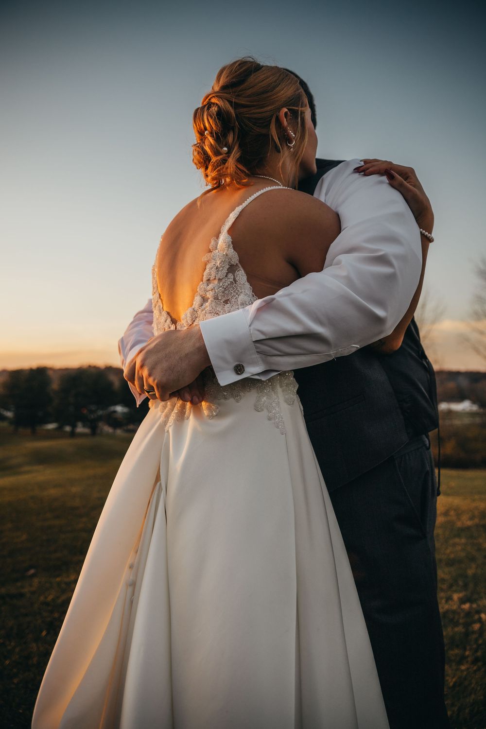 A couple embraces during sunset in a romantic outdoor wedding portrait against a dusky sky.