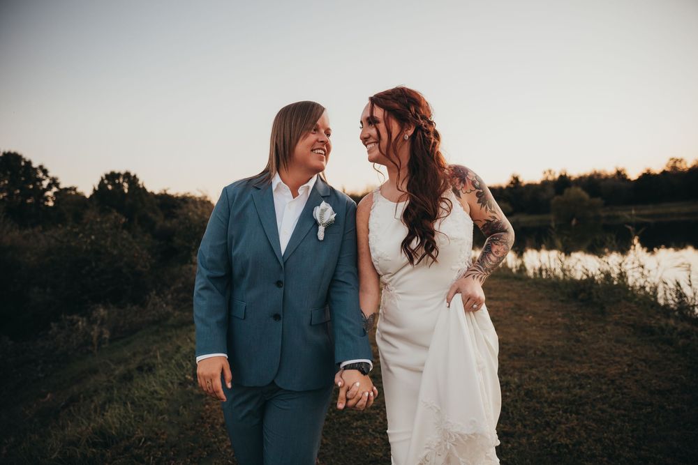 A couple in wedding attire walk together and smile at each other beside a lake at sunset. Midwest photographer vigo parke Clay County terre