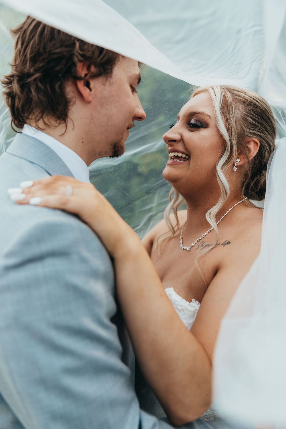 A romantic wedding photo capturing a tender moment between newlyweds under a white veil with mountains in the background.