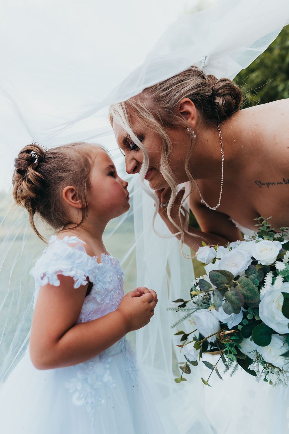 A sweet candid moment showing affection between two dress wearers with white flowers and greenery bouquet at a wedding.